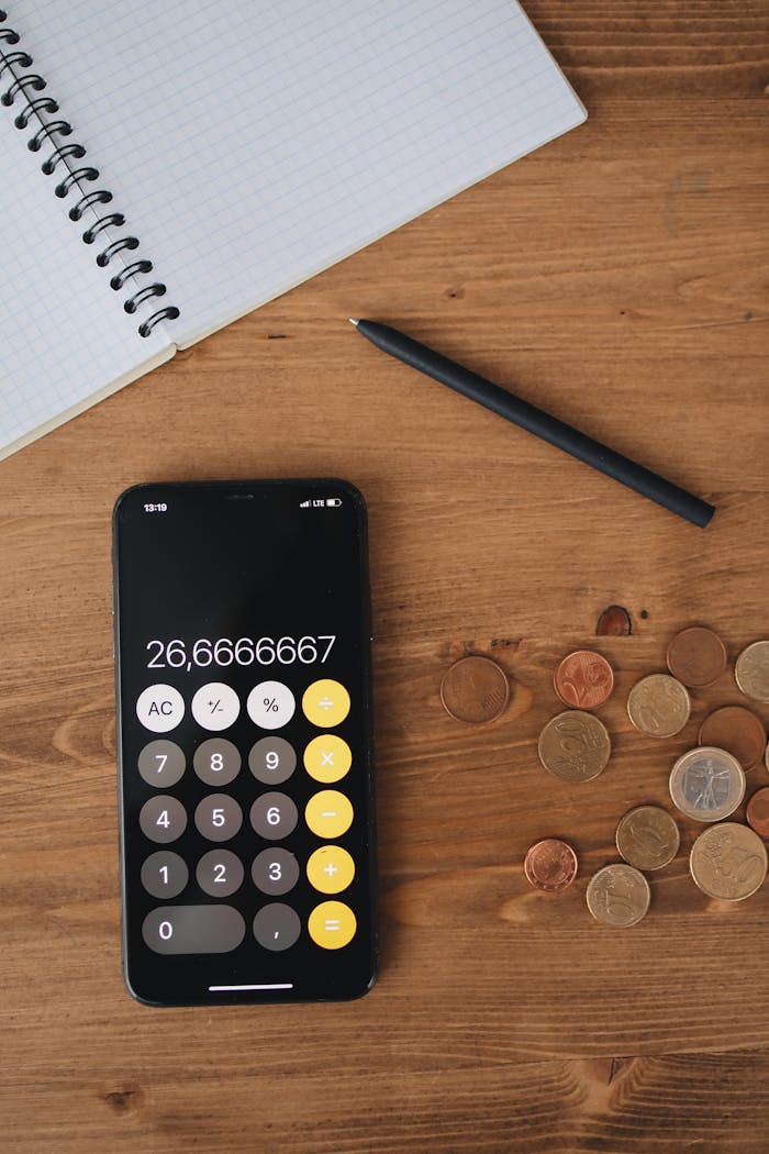Mastering the First Impression: Your intriguing post title goes here Top view of a smartphone calculator, coins, notebook, and pen on a wooden table for financial concept.